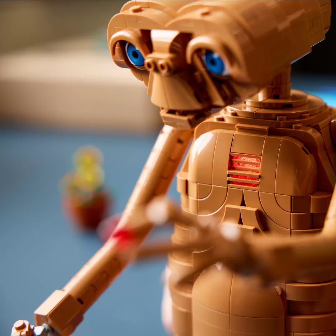 LEGO E.T. figure with tan brick construction, blue eyes, and illuminated red chest piece against blue background.