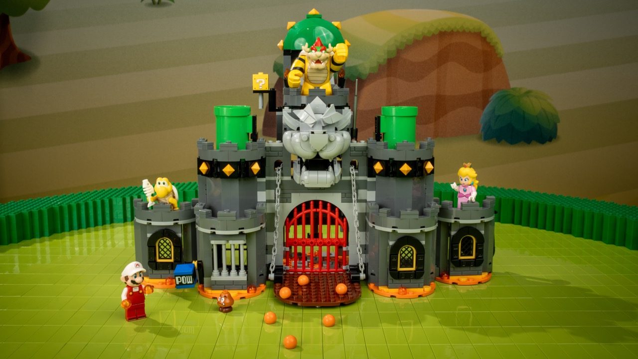 LEGO Super Mario castle set with Bowser figure, Princess Peach minifigure, and orange lava balls on green baseplate.