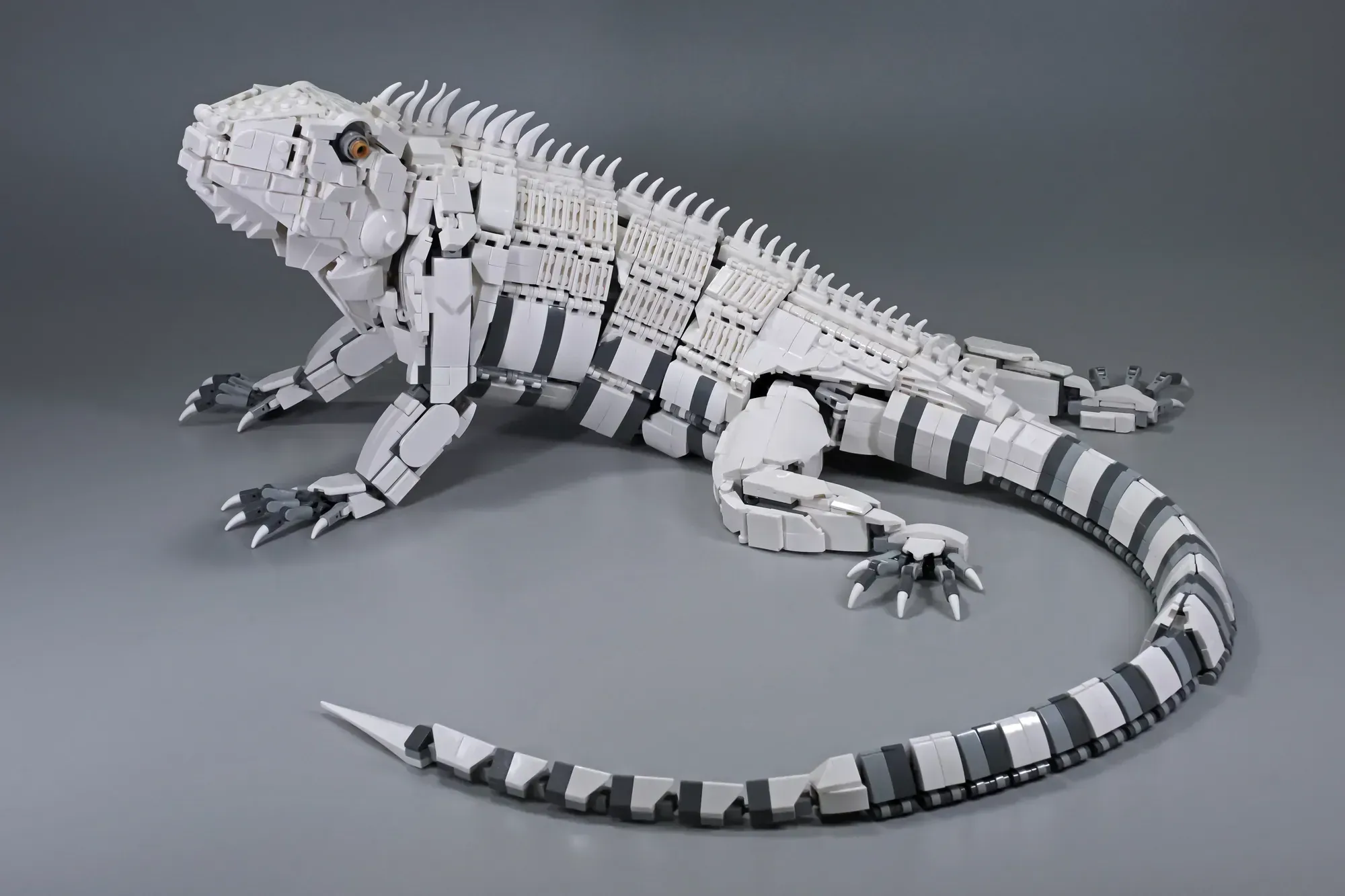 LEGO robotic iguana model with segmented white and gray body, articulated limbs, and detailed tail on gray surface.