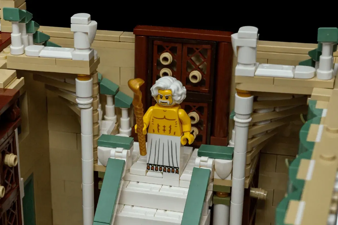 LEGO minifigure in yellow robes with white hair stands in ornate entrance hall of ancient library building.
