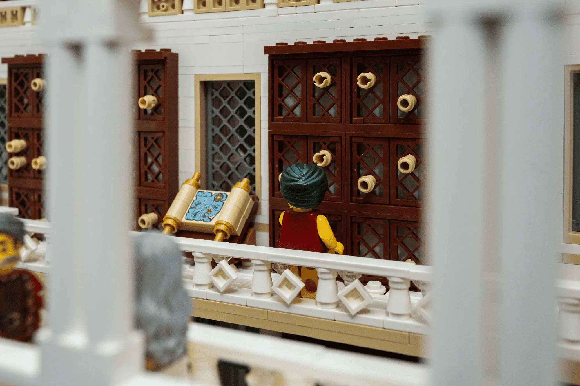 LEGO minifigure studying scrolls before ornate wooden doors with gold ring handles in ancient library setting.