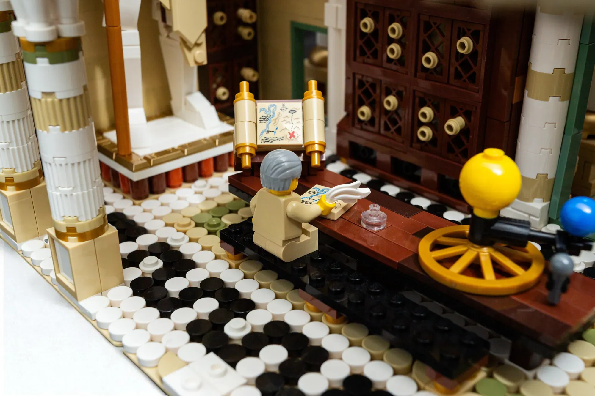 LEGO Ancient Library scene with minifigure scholar at desk, scrolls, globe, and classical architecture on mosaic floor.