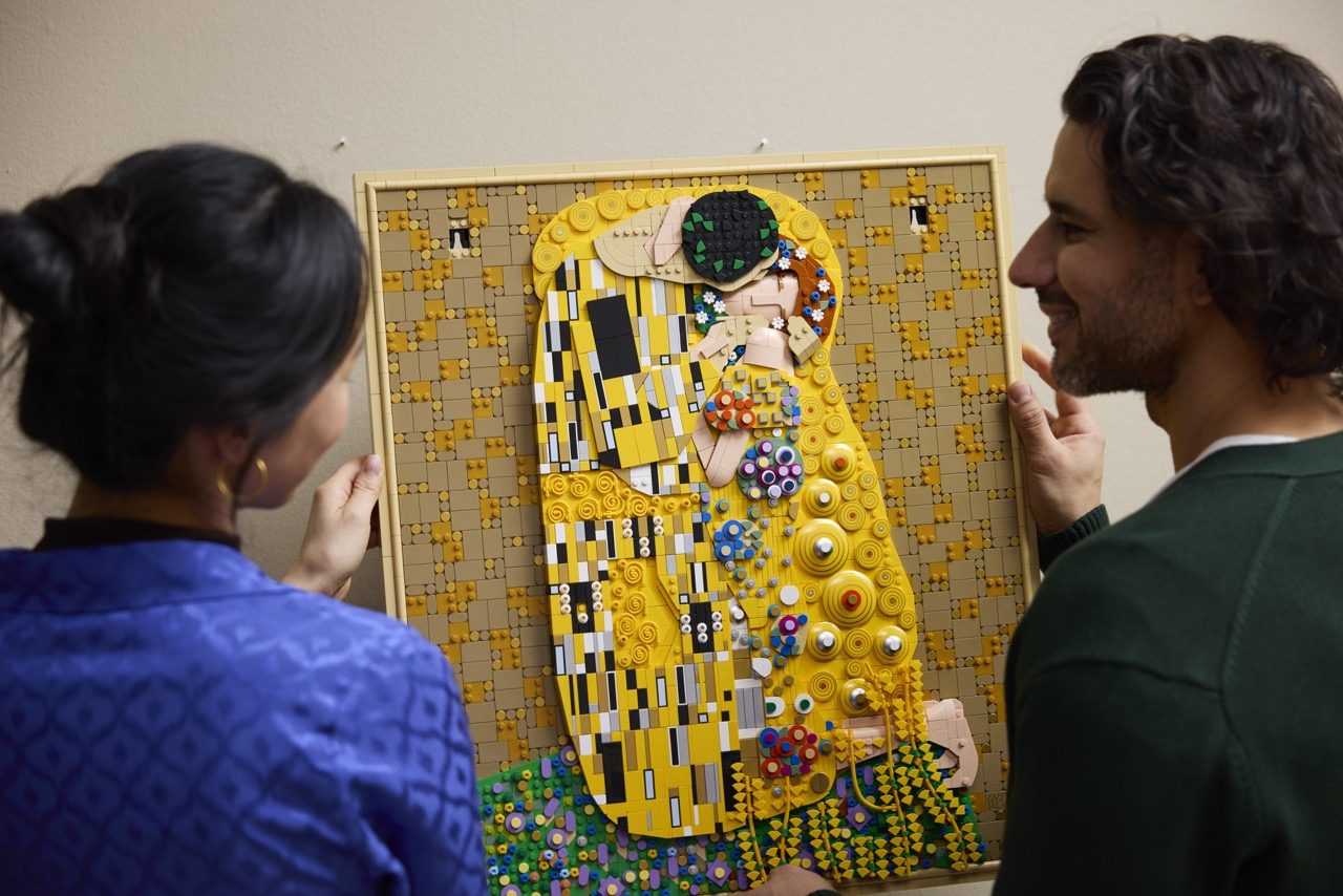 Two people admire a large LEGO Art mosaic recreating Gustav Klimt's "The Kiss" with yellow, gold, and colorful decorative …