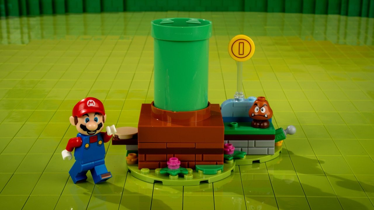 LEGO Super Mario set with Mario minifigure, green pipe, Goomba enemy, and brown brick platform on yellow baseplate.
