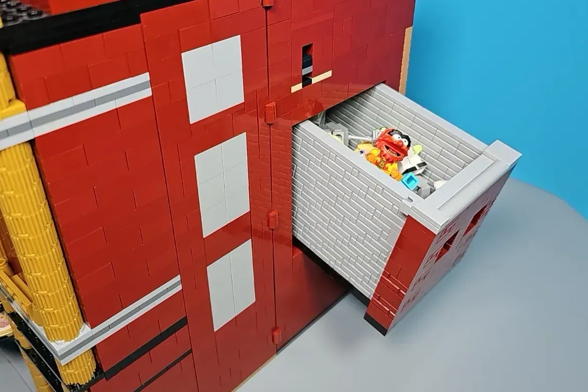 LEGO Muppet Theatre red brick building with minifigure on rooftop against blue background.