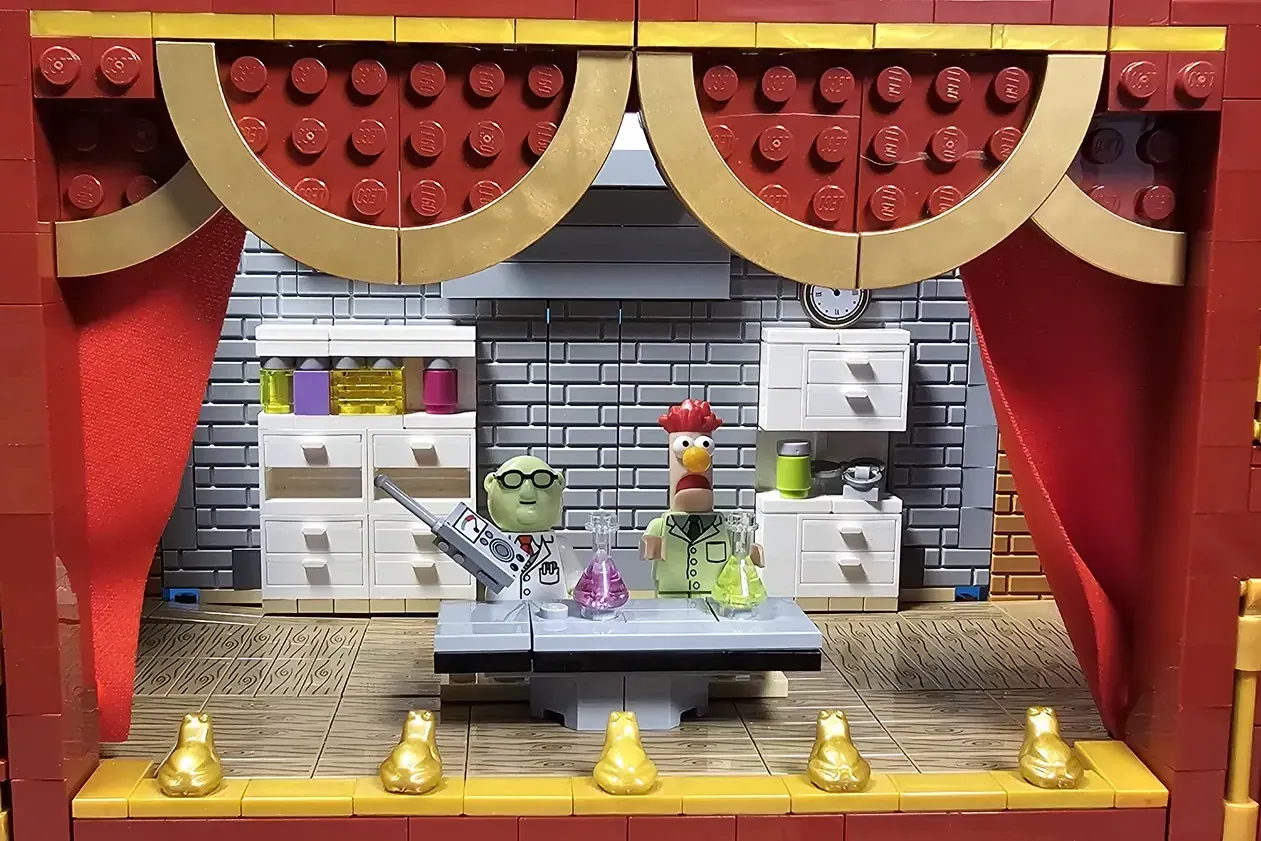 LEGO Muppet Theatre set with red curtains, gold trim, and minifigures of Bunsen Honeydew and Beaker at laboratory counter.