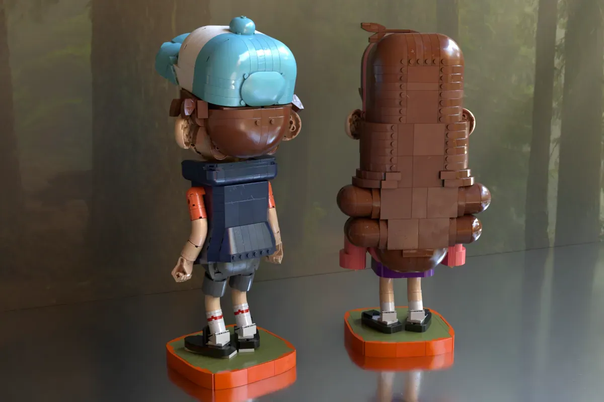 Two LEGO brick figures of Mabel and Dipper from Gravity Falls displayed on orange bases, shown from front and back views.