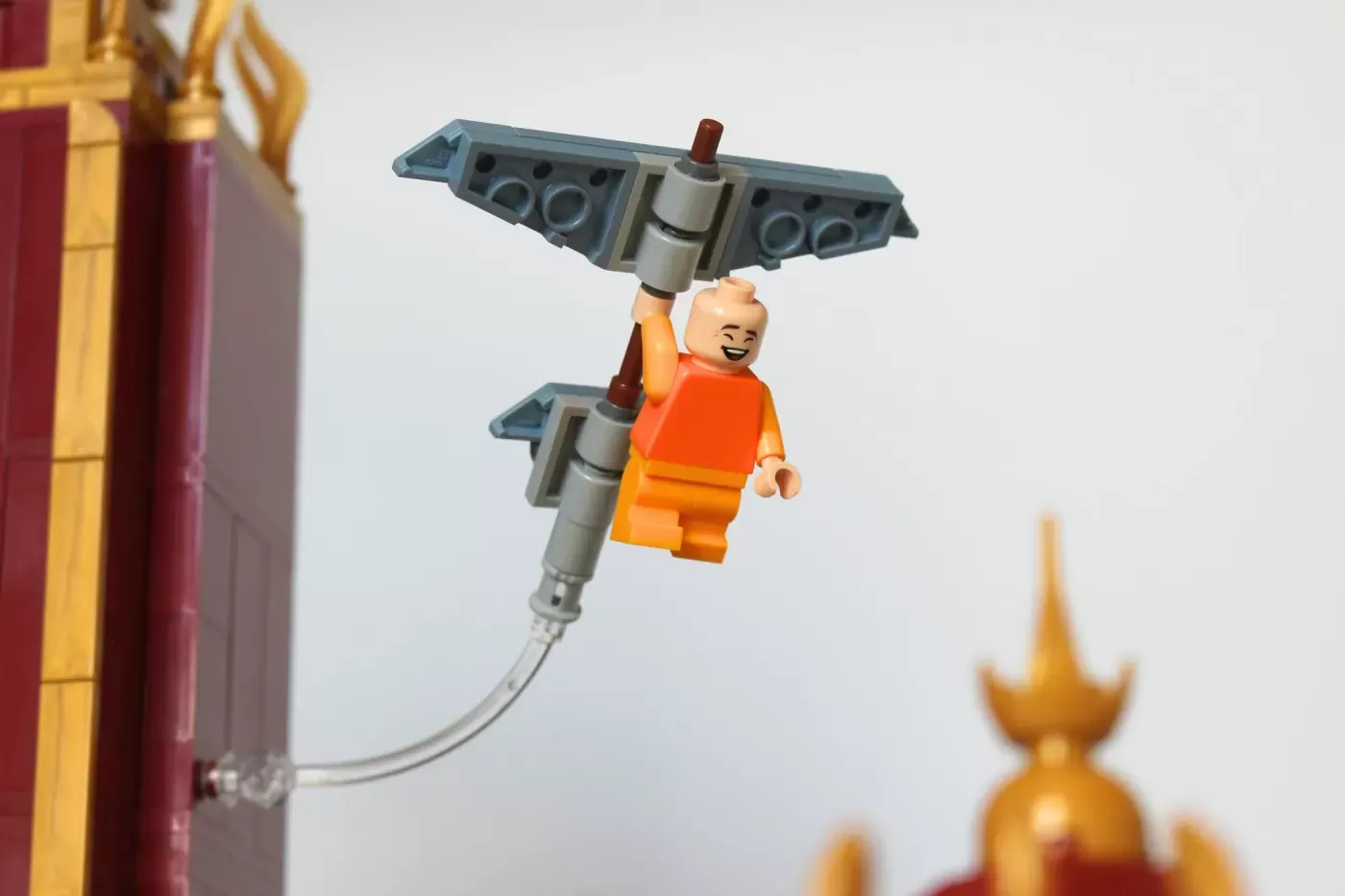 LEGO minifigure in orange outfit flying with rocket pack near Fire Nation Palace architecture.