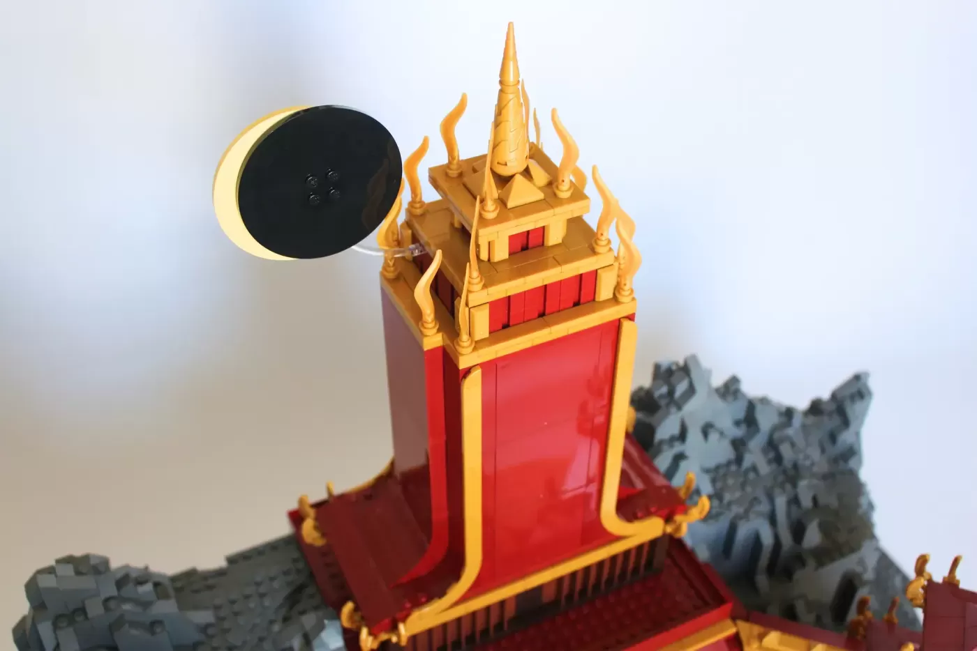 LEGO Fire Nation Palace with golden spires, red walls, flame details, and moon accessory on gray rocky base.