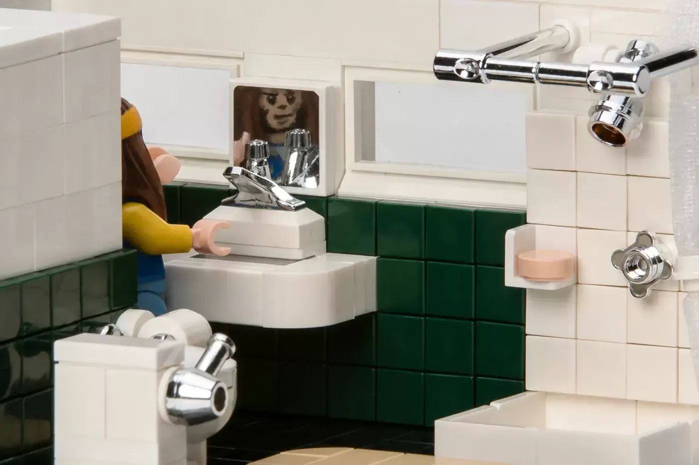 LEGO bathroom scene with minifigure in yellow shirt at sink with green and white tiled walls.