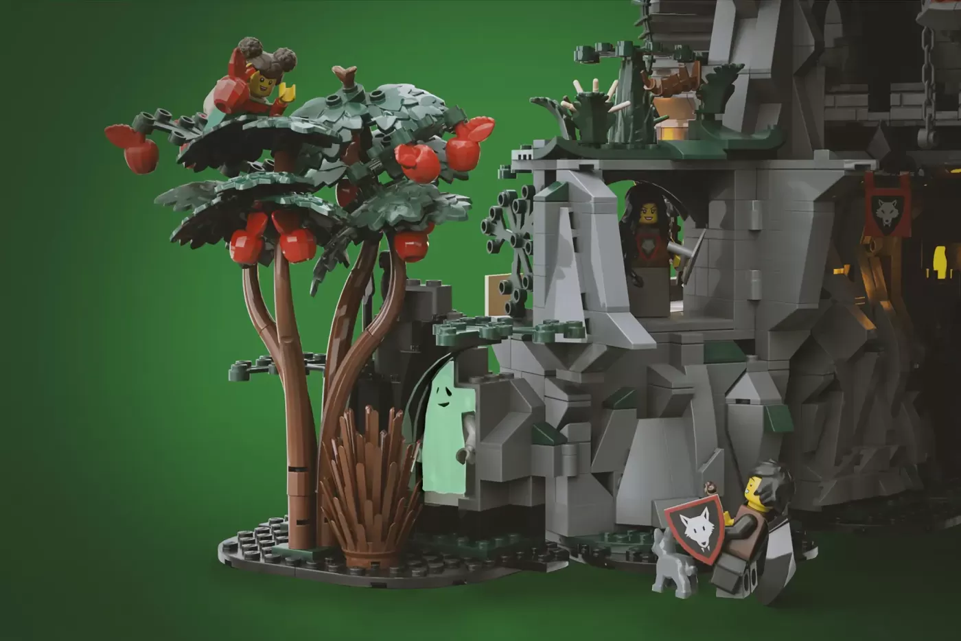 LEGO castle set featuring stone wolf architecture, fruit tree, minifigures, and detailed fortress structures against green…